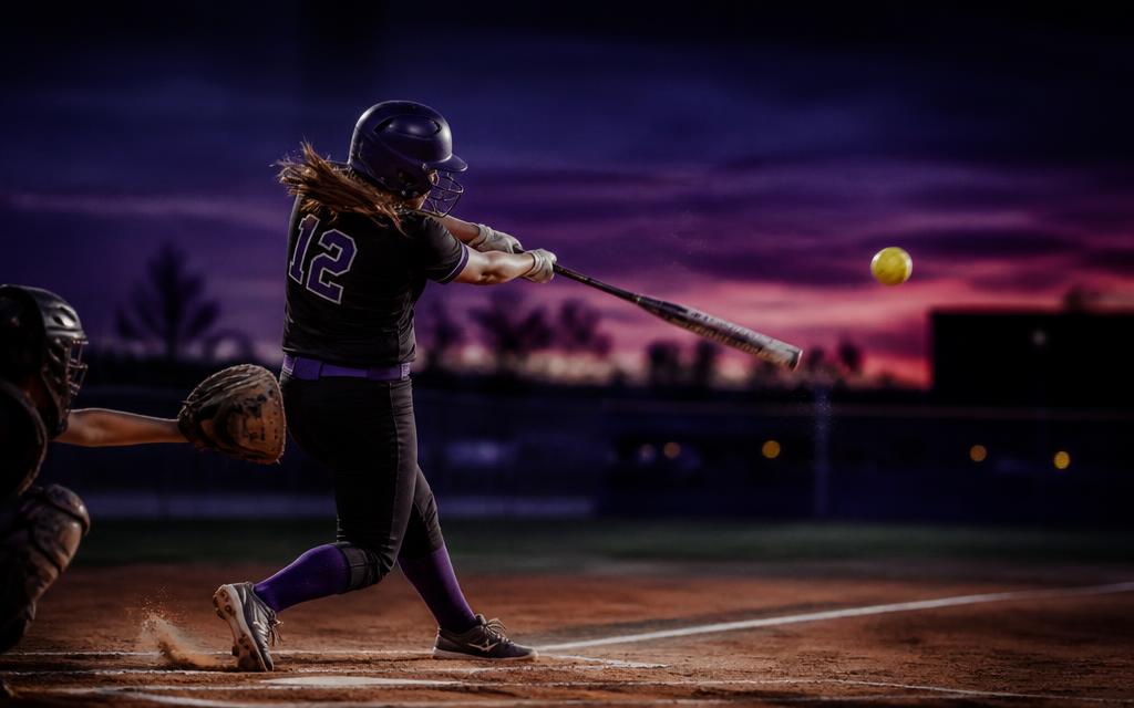 Softball player swinging at dusk